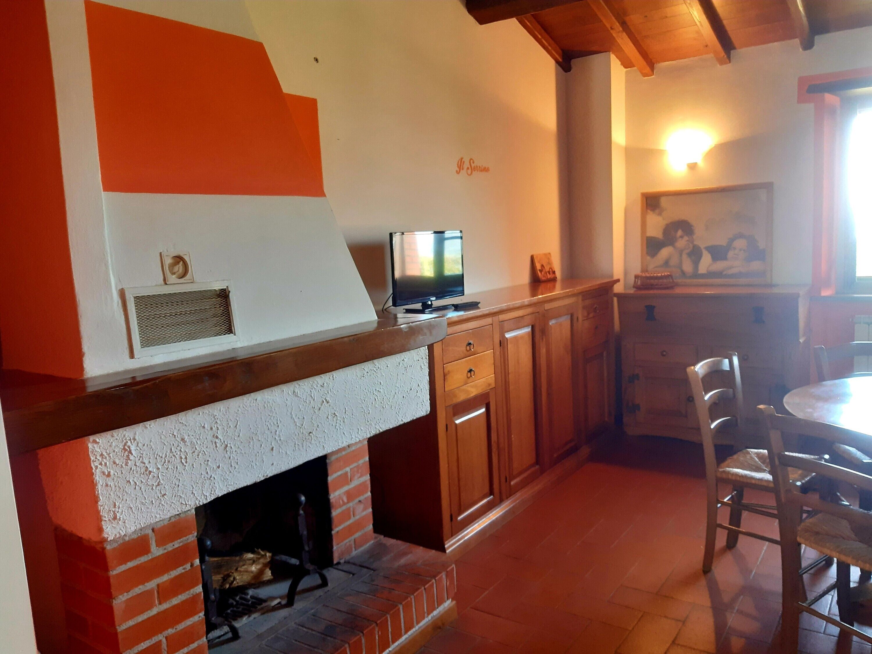 Una cucina con camino in mattoni, mobili in legno, una televisione e un'area pranzo con sedie.