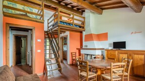 Un comedor con mesa y sillas de madera, una cocina con televisor, y un dormitorio estilo altillo con literas.