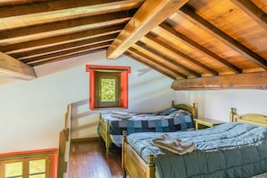 A room with wooden beams, two beds, a window, and a small table.