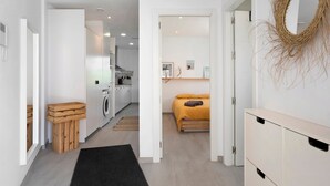 Un interior moderno con una cocina, una cama con cabecera amarilla y un banco de madera.