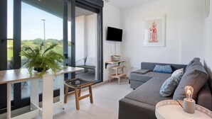 Una sala moderna con sofá, televisión, planta y balcón con vistas.