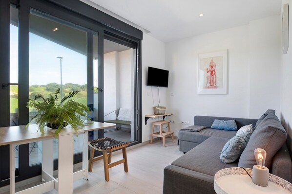 A modern living room with a sofa, a television, a plant, and a balcony with a view.