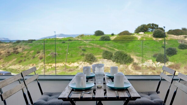 Una mesa de comedor con platos, tazas y una jarra de vidrio, frente a una vista panorámica de colinas y árboles verdes.