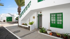 Un edificio blanco con detalles verdes, una palmera y plantas en macetas.