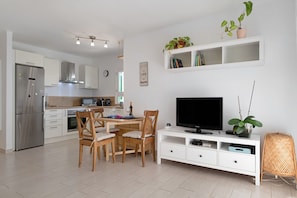 A modern kitchen with a dining area, a flat-screen TV, and a bookshelf.
