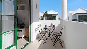 Un balcón con una mesa, sillas, una planta en maceta y una pared blanca.