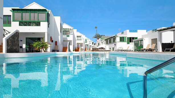 Una piscina con agua azul cristalina, rodeada de edificios blancos con detalles verdes y numerosas ventanas.