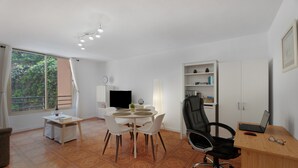 Una habitación con una mesa de comedor, sillas, un televisor, una estantería y un escritorio con una computadora portátil.
