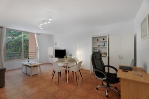 Une pièce comprenant une table à manger, des chaises, un téléviseur, une bibliothèque et un bureau avec un ordinateur portable.