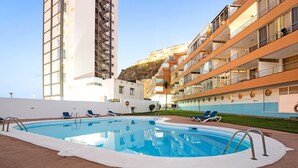 Una piscina con sillones de descanso, un edificio blanco y una estructura alta con balcones.