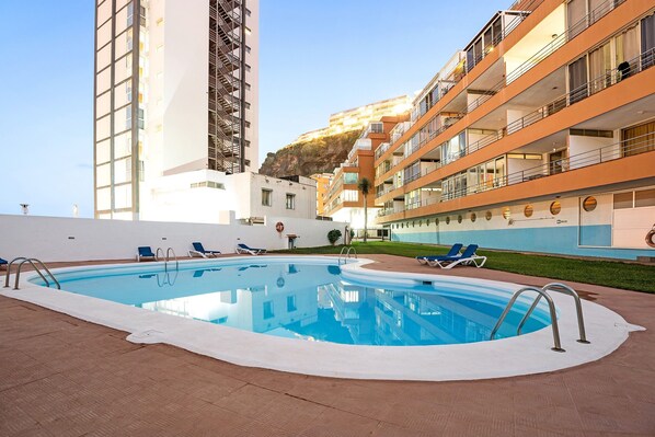 A swimming pool with lounge chairs, a white building, and a tall structure with balconies.