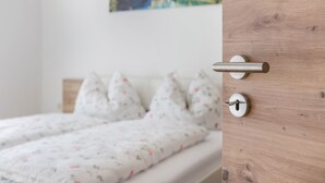 A bed with a floral-patterned bedspread, a wooden door with a handle, and a wall-mounted picture. - Apartment "Trojer 2" with Mountain View, Whirlpool & Wi-Fi (Sarentino)