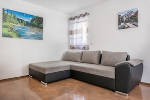 A corner room with a sectional sofa, a window with curtains, and two wall-mounted paintings.