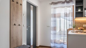 A room with a wooden bench, a door, a curtain, and a kitchen area with a plant and fruit bowl. - Apartment "Trojer 2" with Mountain View, Whirlpool & Wi-Fi (Sarentino)