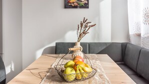 Una mesa de comedor con una cesta de frutas, un jarrón con plantas secas y un cuadro en la pared.