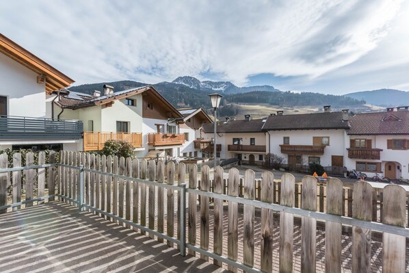 A residential area with a wooden fence, houses with balconies, and a mountain backdrop. - Apartment "Trojer 1" with Mountain View, Balcony & Wi-Fi (Sarentino)