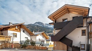 Edificio residencial con escaleras, balcones de madera y un paisaje montañoso al fondo.