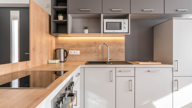 Una cocina moderna con encimera de madera, electrodomésticos de acero inoxidable y muebles grises.