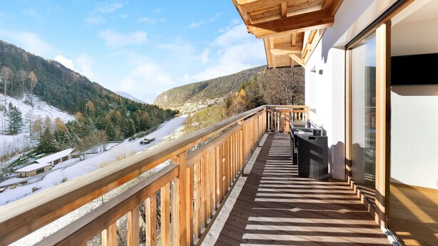 Ein Holzbalkon mit Blick auf ein verschneites Tal und Berge.