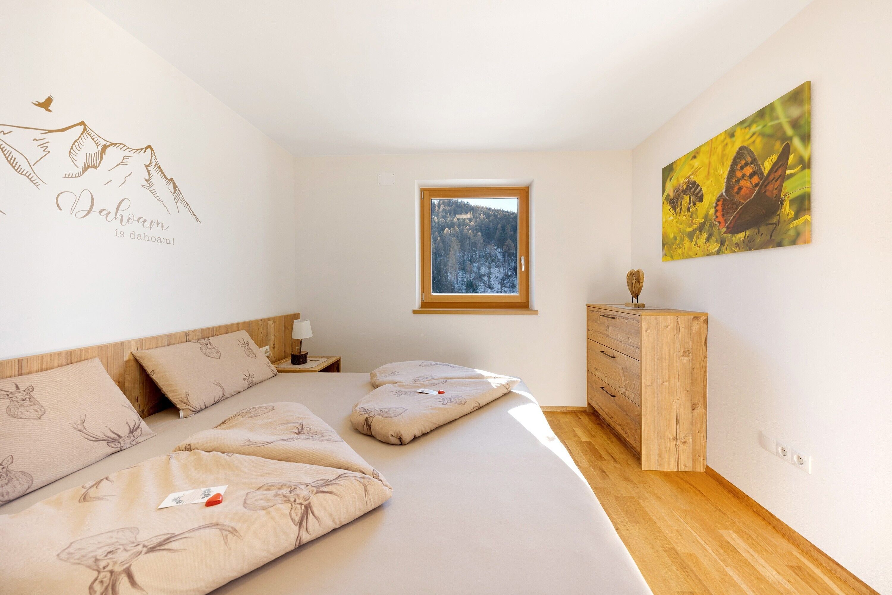 Une chambre à coucher comprenant un lit, une commode, une fenêtre avec vue et un mur orné d’une illustration de montagne.