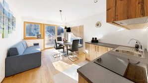 Eine moderne Küche mit Einbauofen, ein Essbereich mit Tisch und Stühlen sowie ein Sofa in einem Wohnbereich mit großen Fenstern.