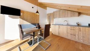 A modern kitchen with wooden cabinets, a dining table with chairs, and a flat-screen TV mounted on the wall. - Töniglerhof  "Apartment Morgensonne" with Mountain View, Garden & Wi-Fi (Trodena)