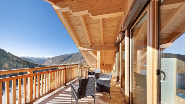 A wooden balcony with a view of mountains, furnished with wicker chairs and a table. - Töniglerhof  "Apartment Morgensonne" with Mountain View, Garden & Wi-Fi (Trodena)