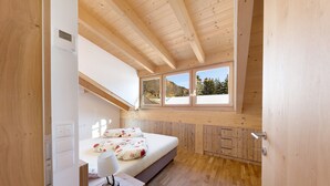A bedroom with a wooden ceiling, a bed with floral bedding, a bedside table with a lamp, and a window with a view of trees. - Töniglerhof  "Apartment Morgensonne" with Mountain View, Garden & Wi-Fi (Trodena)