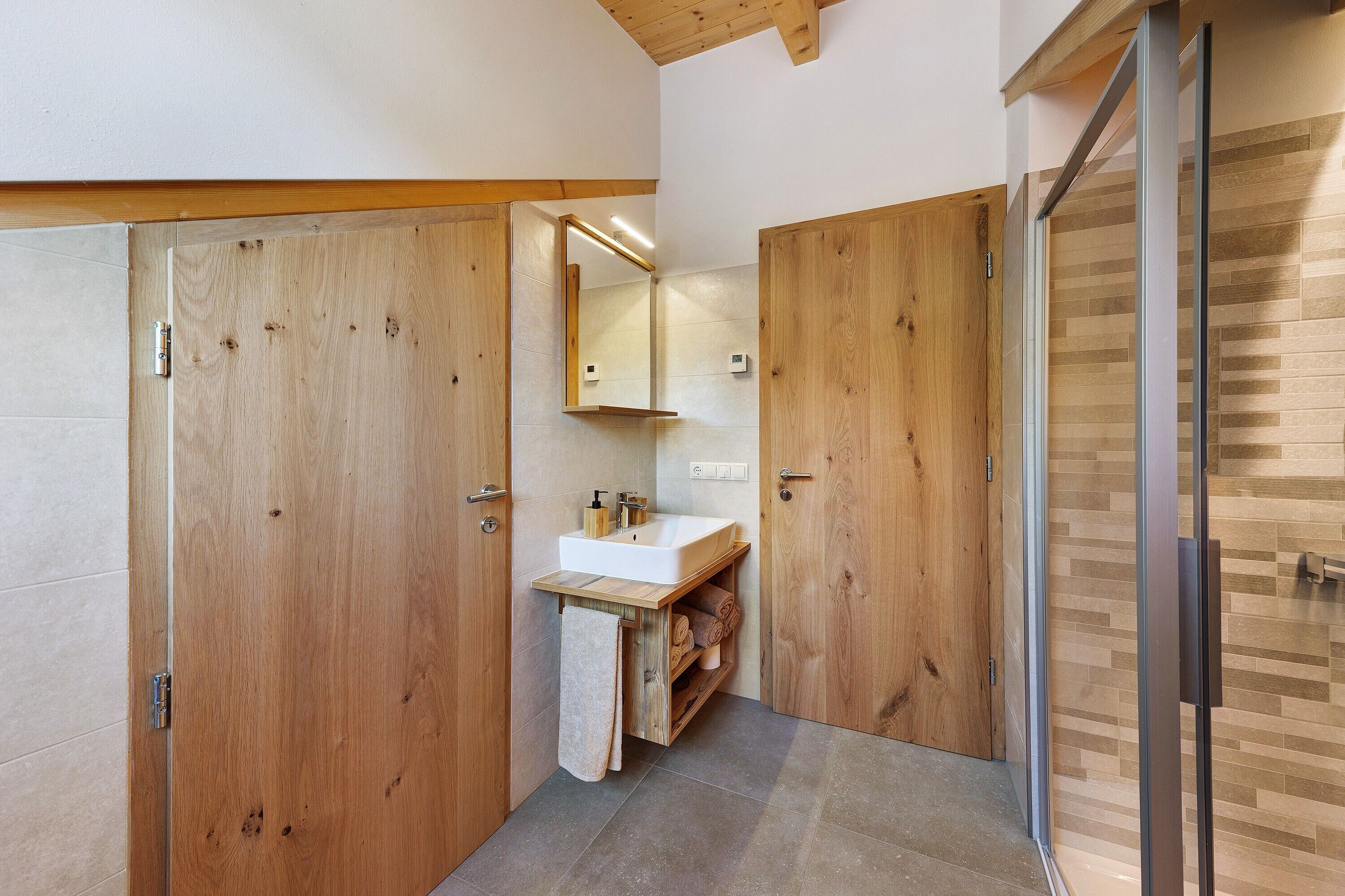 Een moderne badkamer met houten deuren, een witte wastafel en een spiegel.
