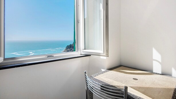 Une pièce avec vue sur l’océan, accessible par une fenêtre, comprenant une chaise et une petite table.