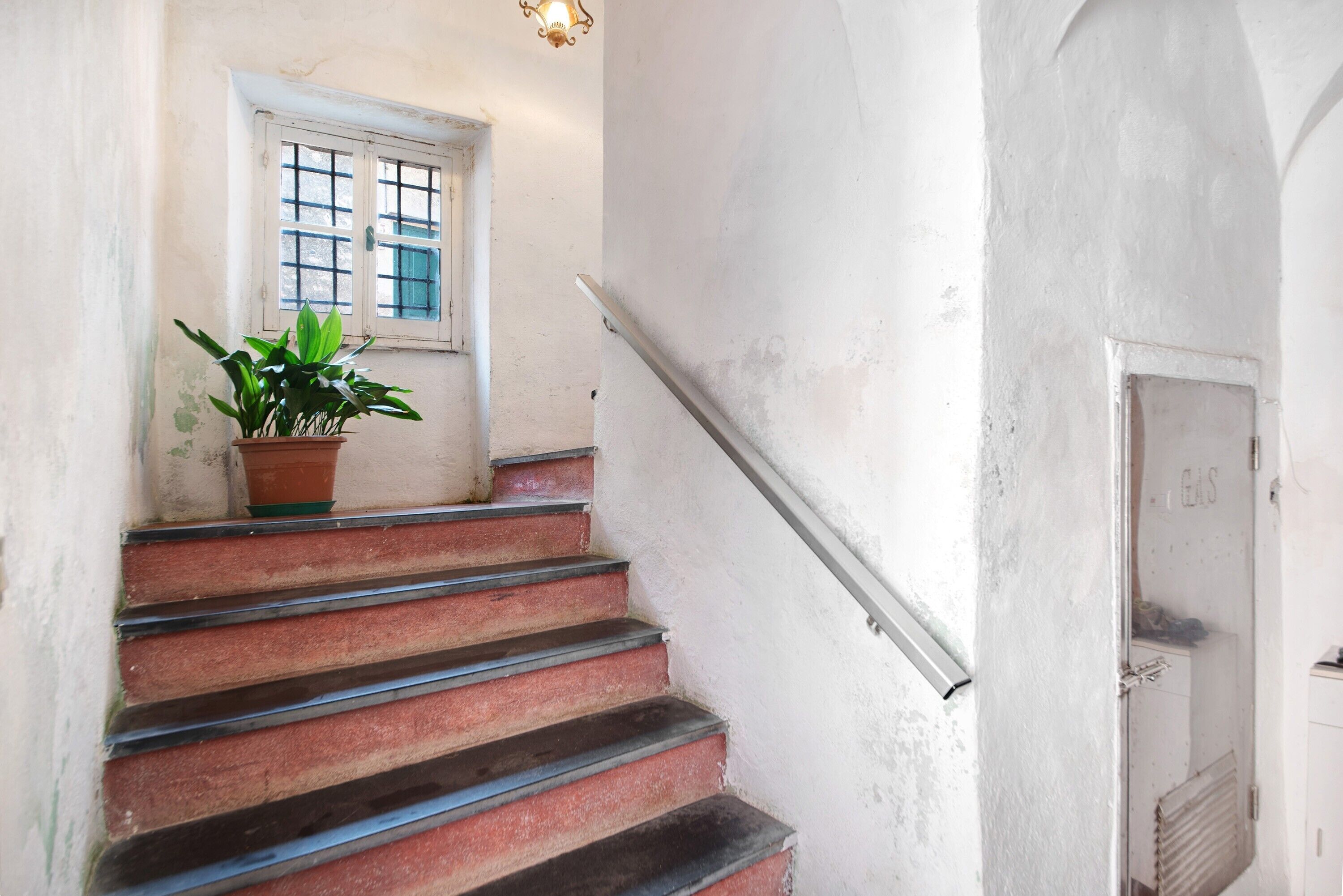 A staircase with a potted plant, a window with grid panes, and a door labeled 'GAS.'