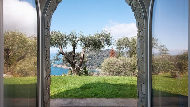 An arched doorway leading to a grassy area with trees and a distant view of a body of water.