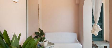 Une pièce avec un canapé blanc, une petite table sur laquelle est posée une plante en pot, un panneau d’accueil et une vue sur l’extérieur.