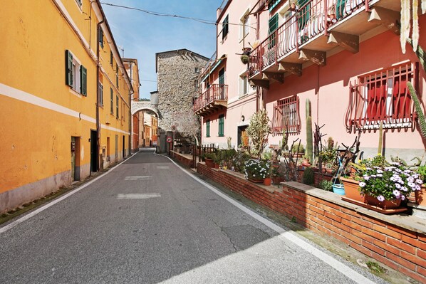 A narrow street lined with colorful buildings, some with balconies and potted plants.