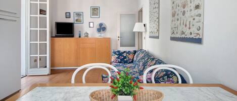 A living room with a TV, a sofa, a dining table, and a wall with nautical-themed artwork.