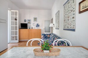 A living room with a TV, a sofa, a dining table, and a wall with nautical-themed artwork.