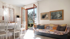 A living room with a sofa, chairs, a dining table, and a view through an open door.