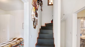 A staircase leading to a bathroom with a tiled wall, a bed with a patterned bedspread, and a wall-mounted shelf with various items.
