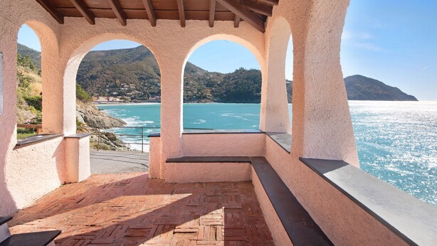 A covered terrace with a view of the sea and a mountainous landscape.