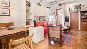 Une pièce chaleureuse comprenant une table à manger, des chaises, un petit meuble blanc, un canapé rouge et une bibliothèque.