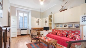 Un salon comprenant un canapé, des fauteuils, une table, un téléviseur et un coin cuisine.