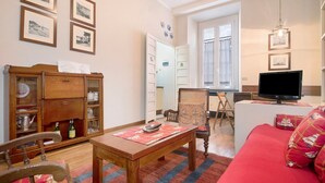 Un salon avec un canapé rouge, une table en bois et un téléviseur. On y trouve également un meuble avec des portes en verre et une chaise.