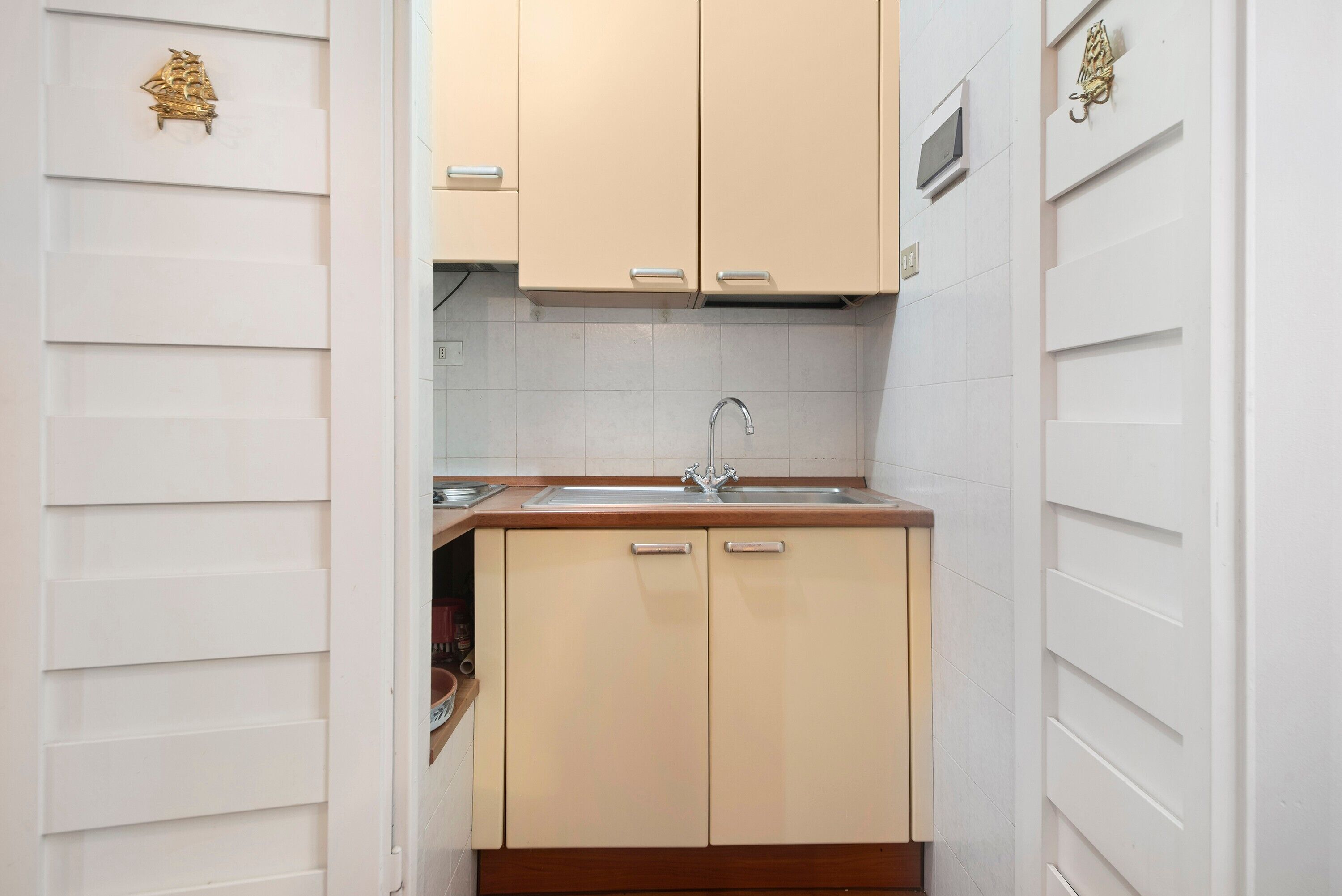 A compact kitchen with a sink, two cabinets, and a small window above the sink.