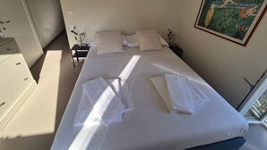Ein Hotelzimmer mit Bett, Kissen, Nachttisch, Kommode und einem Gemälde an der Wand.