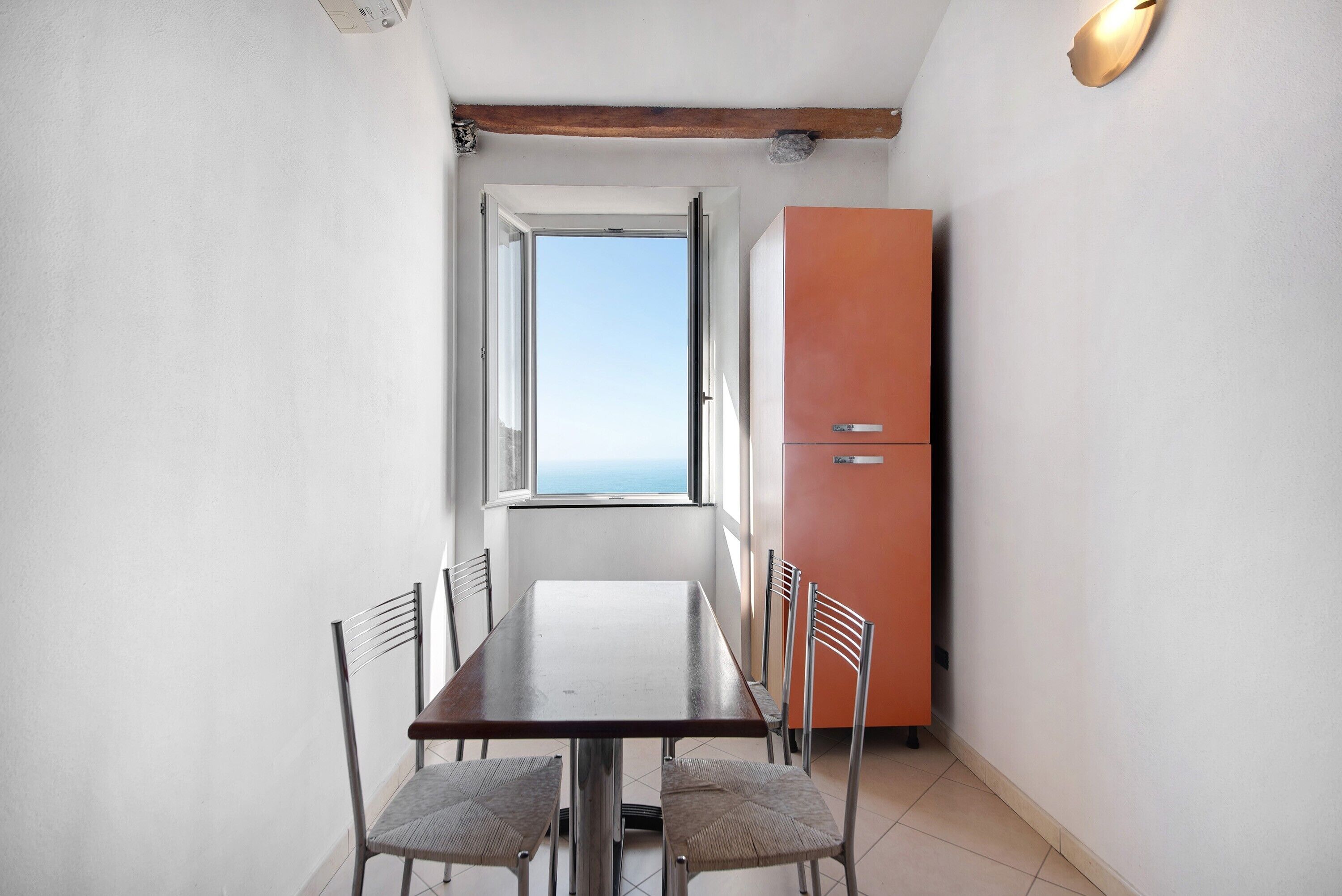 Ein kleiner Raum mit Esstisch, Stühlen, einem Fenster und einem Kühlschrank.