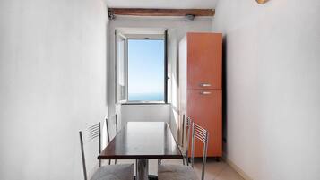 Ein kleiner Raum mit Esstisch, Stühlen, einem Fenster und einem Kühlschrank.