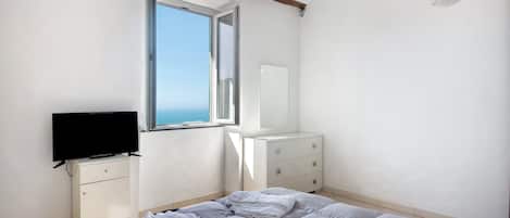 A bedroom with a bed, a TV, a dresser, and a window with a view.