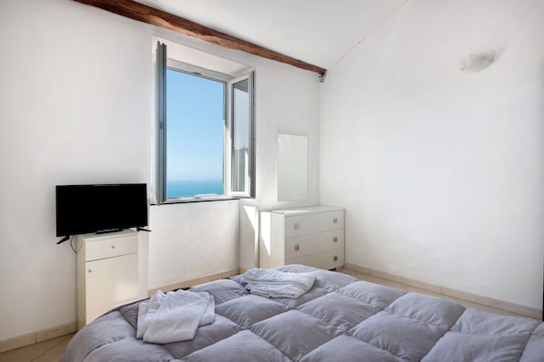 A bedroom with a bed, a TV, a dresser, and a window with a view.