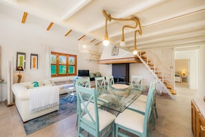 Un vaste espace de vie comprenant une table à manger en verre, des canapés blancs et un escalier menant à un niveau supérieur.