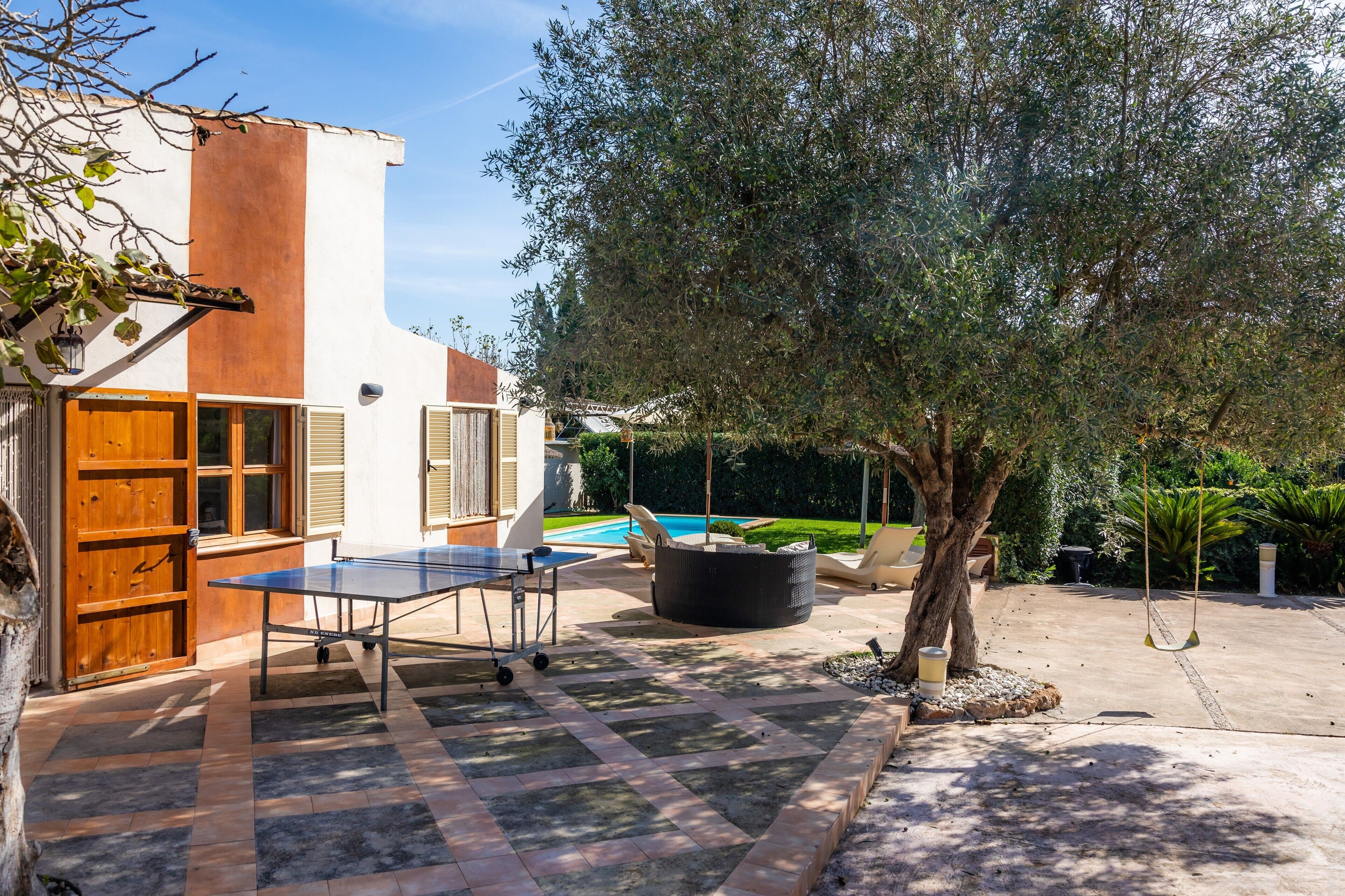 Una casa con mesa de ping pong, piscina y un árbol grande.